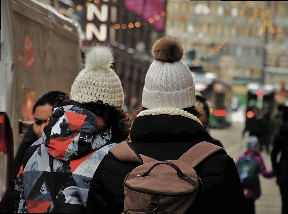 dos chicas con sombreros de lana y mochilas vistas de espaldas en una calle urbana