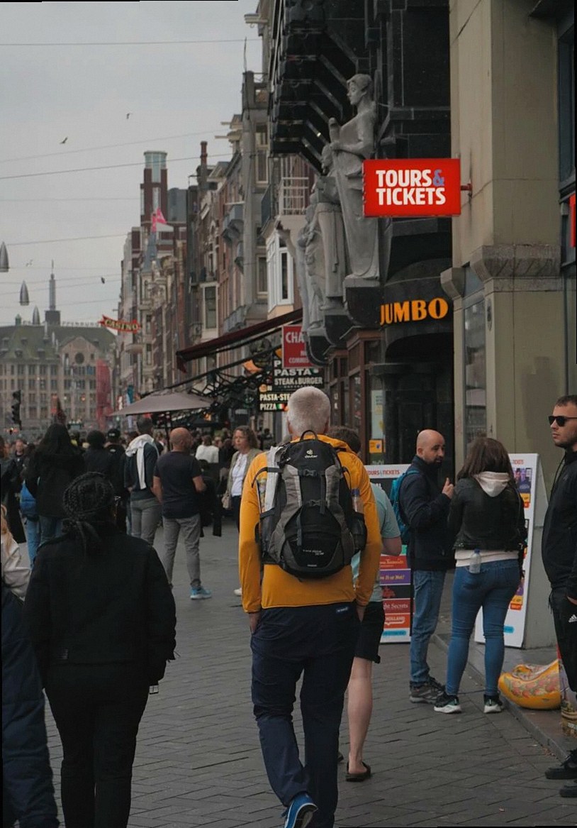Una concurrida calle en Ámsterdam, con turistas, tiendas y arquitectura icónica.